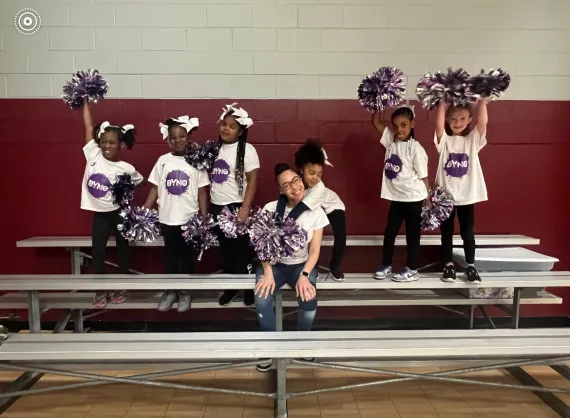 six youth cheer participants posing on bleacher with their coach